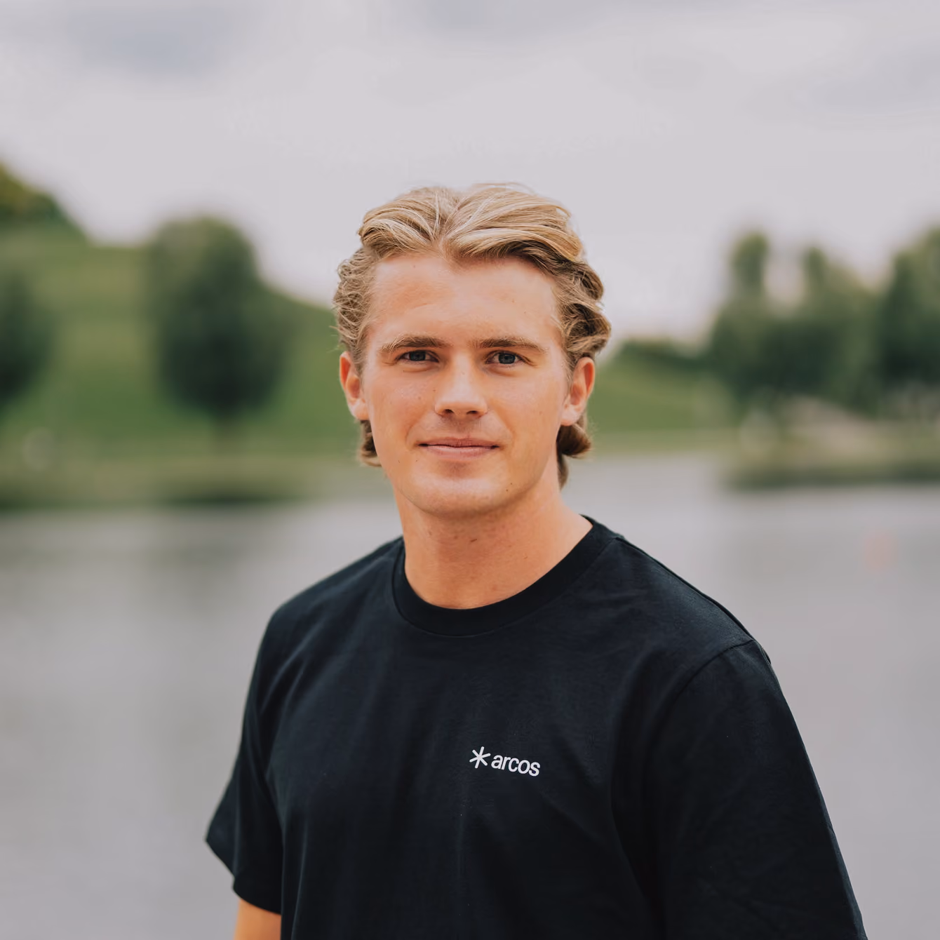Moritz Steigerwald in a black t-shirt in front of a lake.