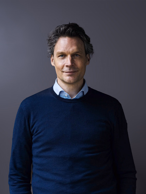 Sebastian Borek in a dark blue sweater against a grey studio background.