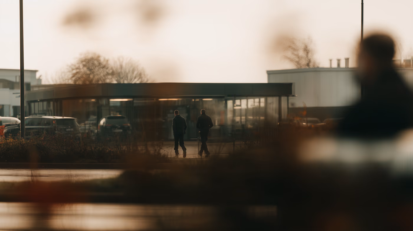 Two people outside a low glass-fronted building at dusk.